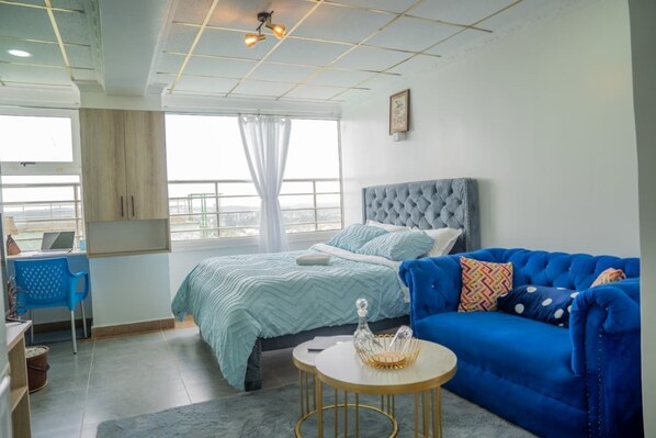 Une chambre à coucher avec un lit, un canapé bleu, une petite table et une fenêtre avec des rideaux.