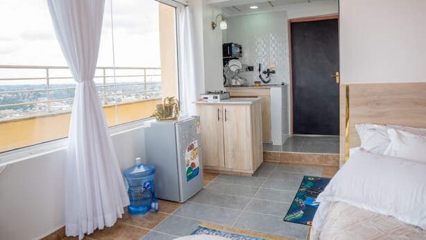Habitación de hotel con cama, una kitchenette pequeña, dispensador de agua y vista a la ciudad.