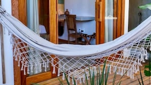 Un hamac sur une terrasse en bois, un coin repas avec une table et des chaises, et une porte-fenêtre coulissante donnant sur une pièce.