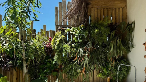 Un bain à remous avec une serviette et des verres à vin, entouré d’une végétation luxuriante et d’une clôture en bois.