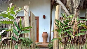 Un sentier de jardin menant à une porte, avec un grand pot et une structure à toit de chaume.