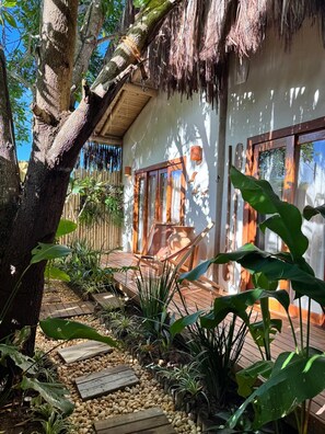 A house with a thatched roof, wooden deck, and a garden with tropical plants. - Casa PreguiƧa (Corumbau)