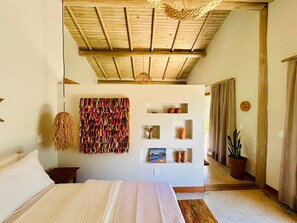 A bedroom with a wooden ceiling, a bed with white linens, a wall-mounted shelf with decorative items, and a hanging woven light fixture. - Casa Preguiça (Corumbau)