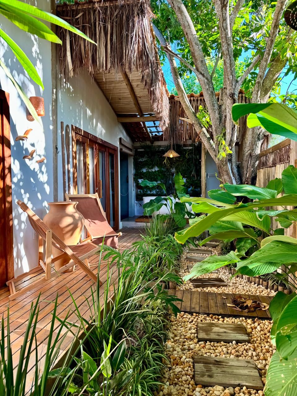 A tropical garden with a wooden deck, a thatched roof structure, and a variety of plants.