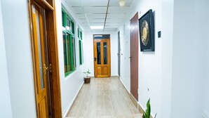 Ein Flur mit Holztüren, Fenstern in grünen Rahmen, einem Topfpflanzen und einem gerahmten Bild an der Wand.
