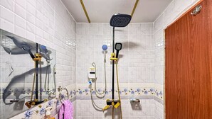 Een badkamer met witte betegelde wanden, een houten deur, een wastafel met spiegel en een douche met een handdouche en een douchekop aan de muur.
