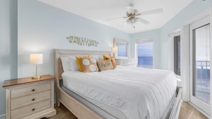 A bedroom with a bed, nightstands, a ceiling fan, and a large window with a view. - Boardwalk 387 (Gulf Shores)