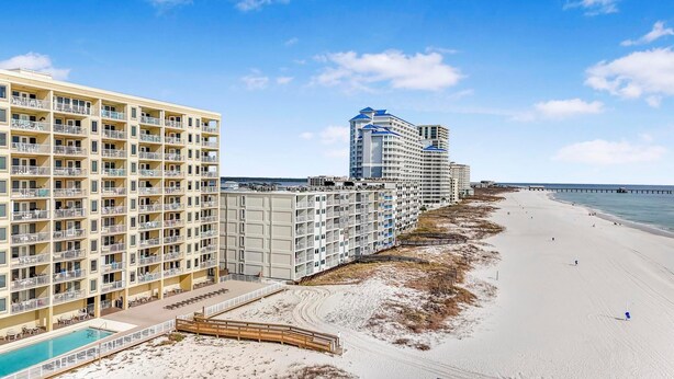 A beachfront hotel with multiple balconies, a swimming pool, and a pier extending into the ocean. - Boardwalk 387 (Gulf Shores)