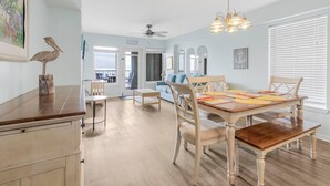 A spacious dining area with a wooden table and chairs, a ceiling fan, and a view of the living room. - Boardwalk 387 (Gulf Shores)