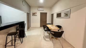 Une cuisine moderne avec un plan de travail noir et des tabourets de bar, un coin repas avec une table en bois et des chaises noires, et un couloir avec une porte et des œuvres d’art accrochées au mur.