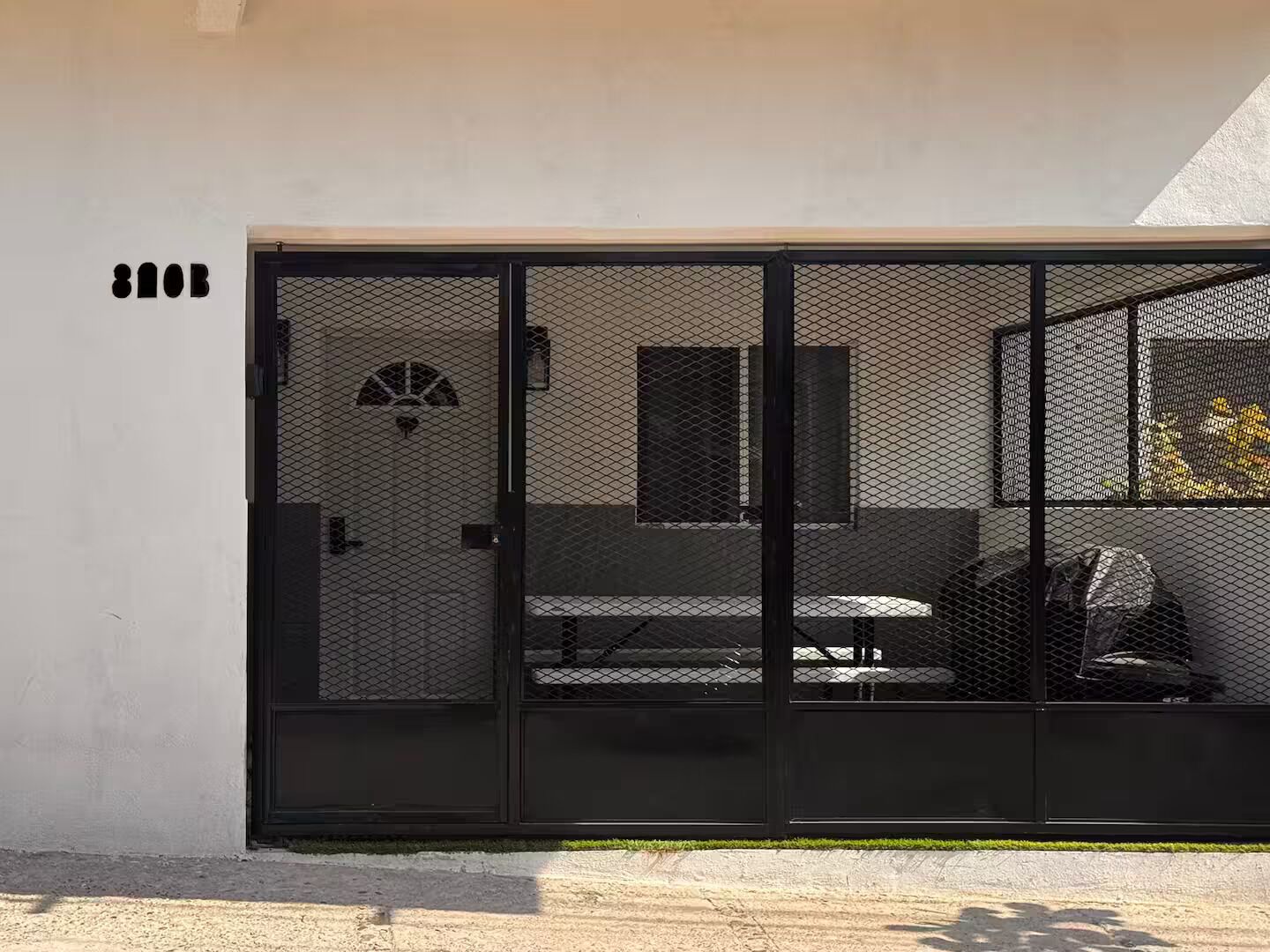 Un bâtiment moderne doté d’un portail en métal noir, d’un banc et d’une petite fenêtre avec un ventilateur.