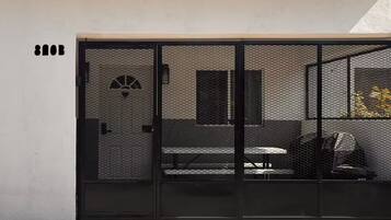 Un bâtiment moderne doté d’un portail en métal noir, d’un banc et d’une petite fenêtre avec un ventilateur.