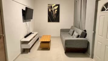 Un salon moderne avec un canapé gris, une table basse en bois, un téléviseur fixé au mur et un tableau encadré accroché au mur.