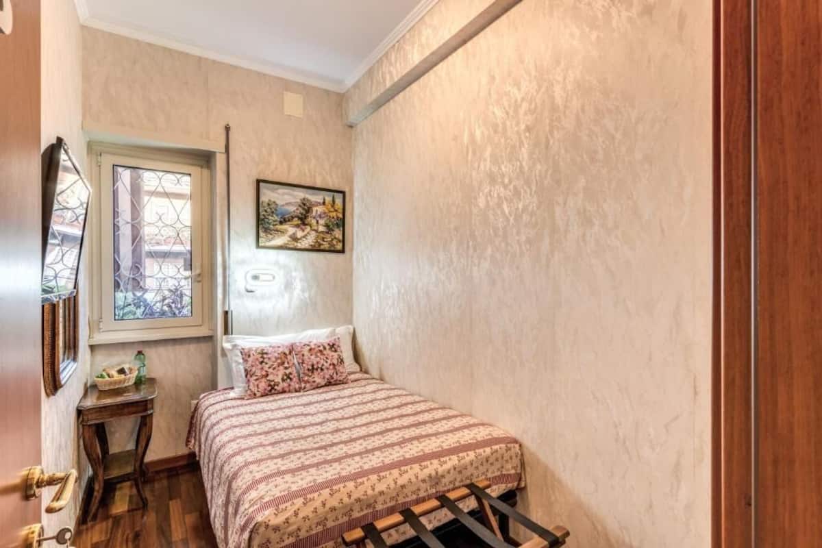 A small bedroom with a bed, a window, a painting, and a wooden door.