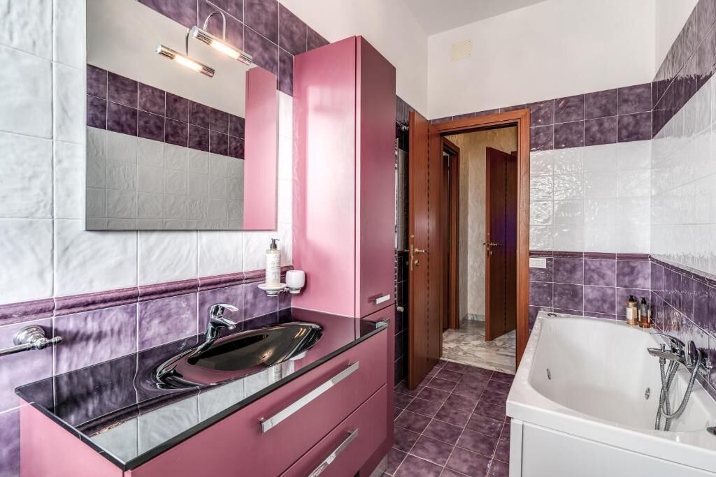 Ein Badezimmer mit einem rosa Waschtisch, einem großen Spiegel, einer weißen Badewanne und lila gefliesten Wänden.