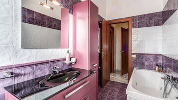 Ein Badezimmer mit einem rosa Waschtisch, einem großen Spiegel, einer weißen Badewanne und lila gefliesten Wänden.