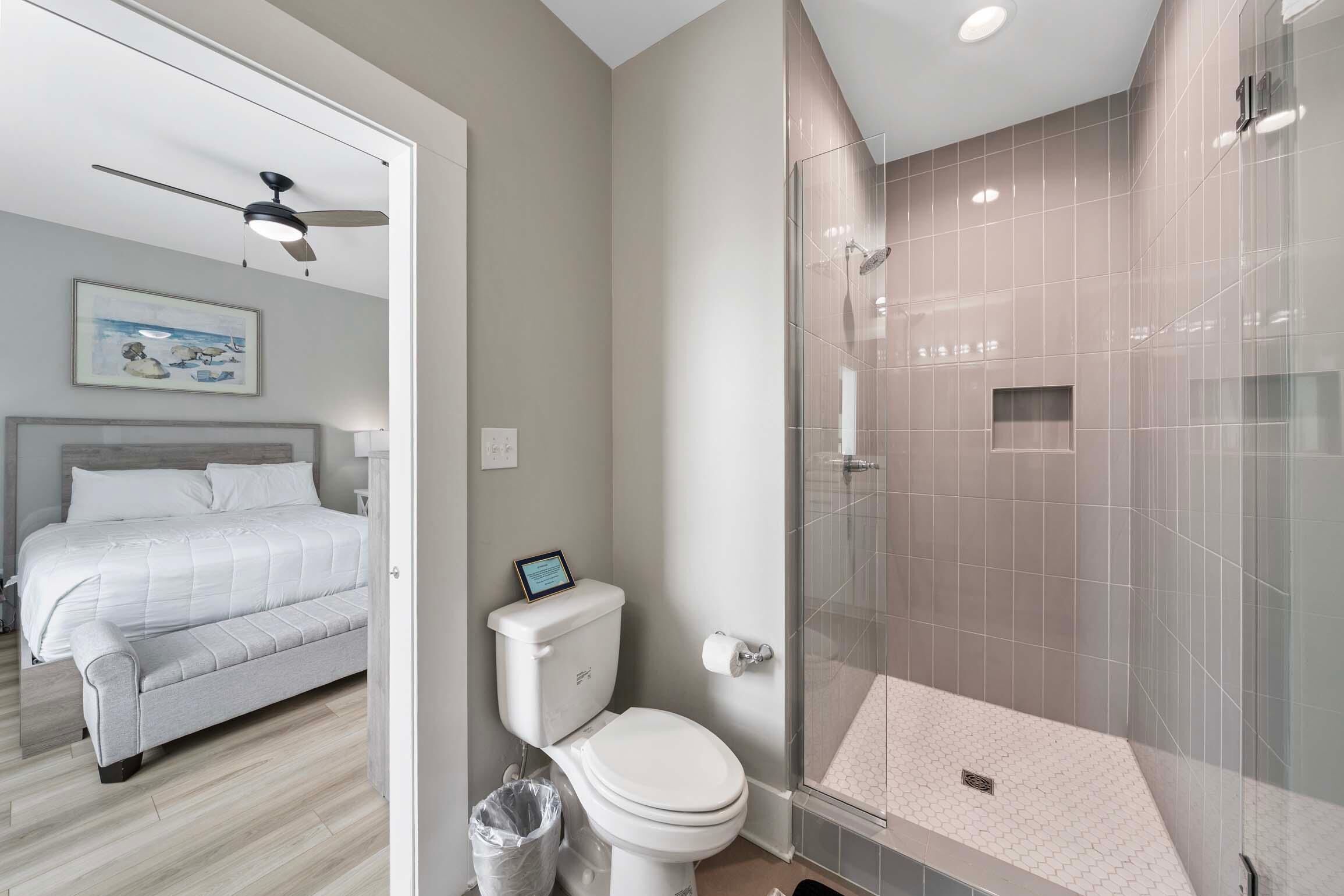 Un baño moderno con cabina de ducha de vidrio, un inodoro y una cama en la habitación contigua.