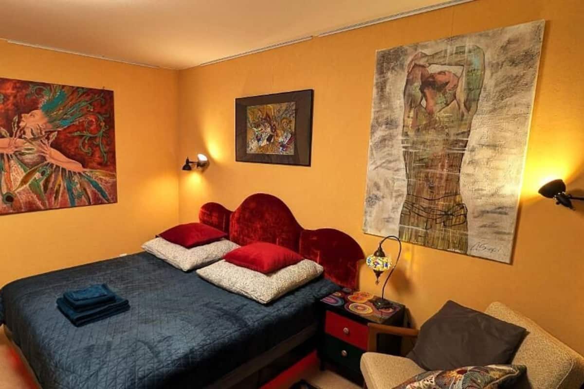 Egy hálószoba, amelyben van egy ágy, két festmény, egy éjjeliszemélyzet és egy szék.
