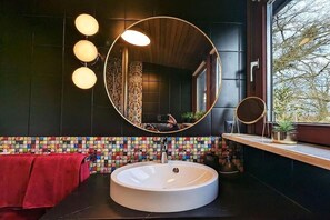 A bathroom with a round mirror, a white sink, and a colorful mosaic backsplash. - Wohnen in der Galerie (Worpswede)