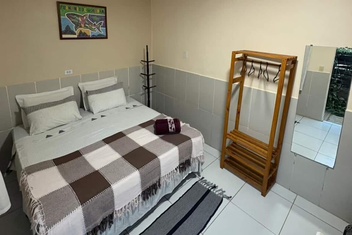 Un dormitorio con cama, una silla de madera, un cuadro y un espejo.