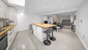A modern kitchen with a wooden island, white cabinetry, and a coffee and tea sign. - Fully Equipped 2BR Flat | Family|Relocations| ST (Greater London)