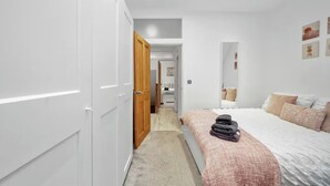 A bedroom with a bed, a wardrobe, a mirror, and a hallway leading to a bathroom. - Fully Equipped 2BR Flat | Family|Relocations| ST (Greater London)