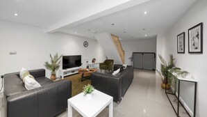 A modern living room with a sofa, a coffee table, a TV, and a staircase leading to another room. - Fully Equipped 2BR Flat | Family|Relocations| ST (Greater London)