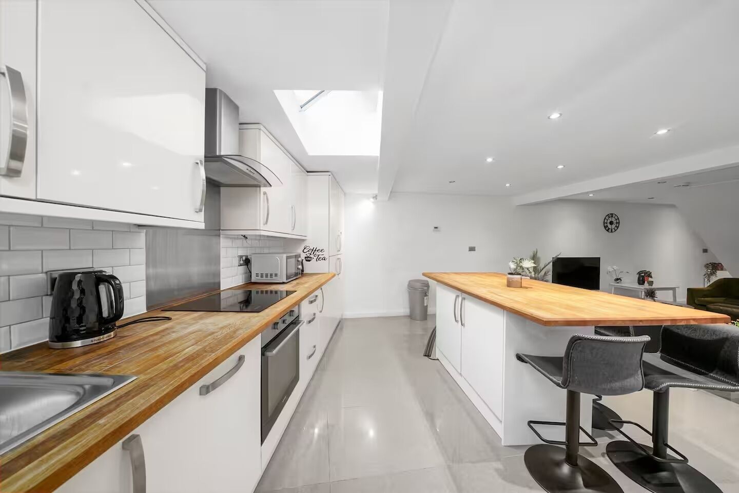 A modern kitchen with white cabinets, a wooden countertop, a kettle, a microwave, and a stove.