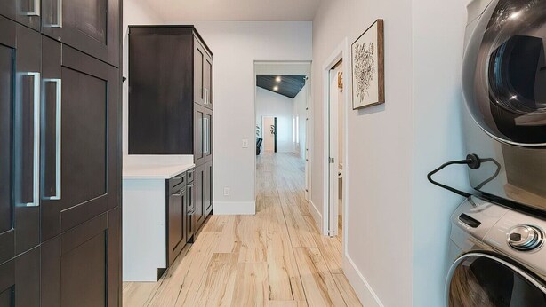 A modern kitchen with dark cabinetry, a wooden floor, and a visible laundry area. - New! Sunset Acres ~ Ideal for all Occasions! (Clermont)