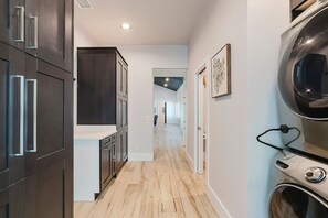A modern kitchen with dark cabinetry, a wooden floor, and a visible laundry area. - New! Sunset Acres ~ Ideal for all Occasions! (Clermont)