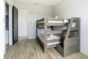 Una cama litera con escalera, una puerta blanca y suelo de madera.