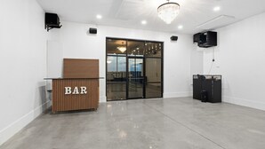 A modern bar area with a wooden counter labeled 'BAR', a glass door leading outside, and a black speaker system on the wall. - New! Sunset Acres ~ Ideal for all Occasions! (Clermont)