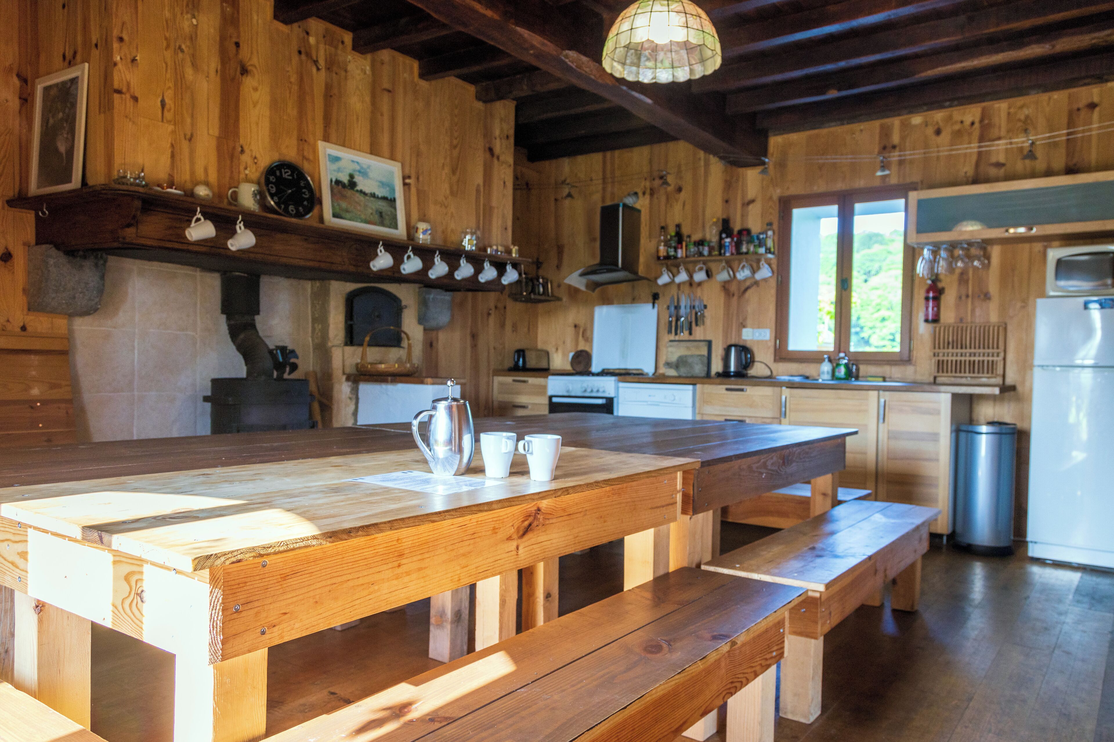 A rustic wooden kitchen with a wooden table and benches, a stove, and various kitchen appliances.