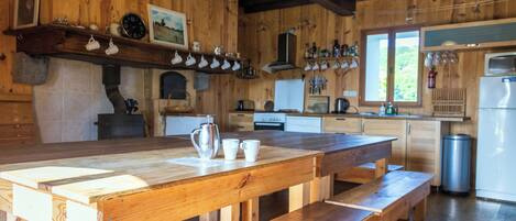 A rustic wooden kitchen with a wooden table and benches, a stove, and various kitchen appliances.