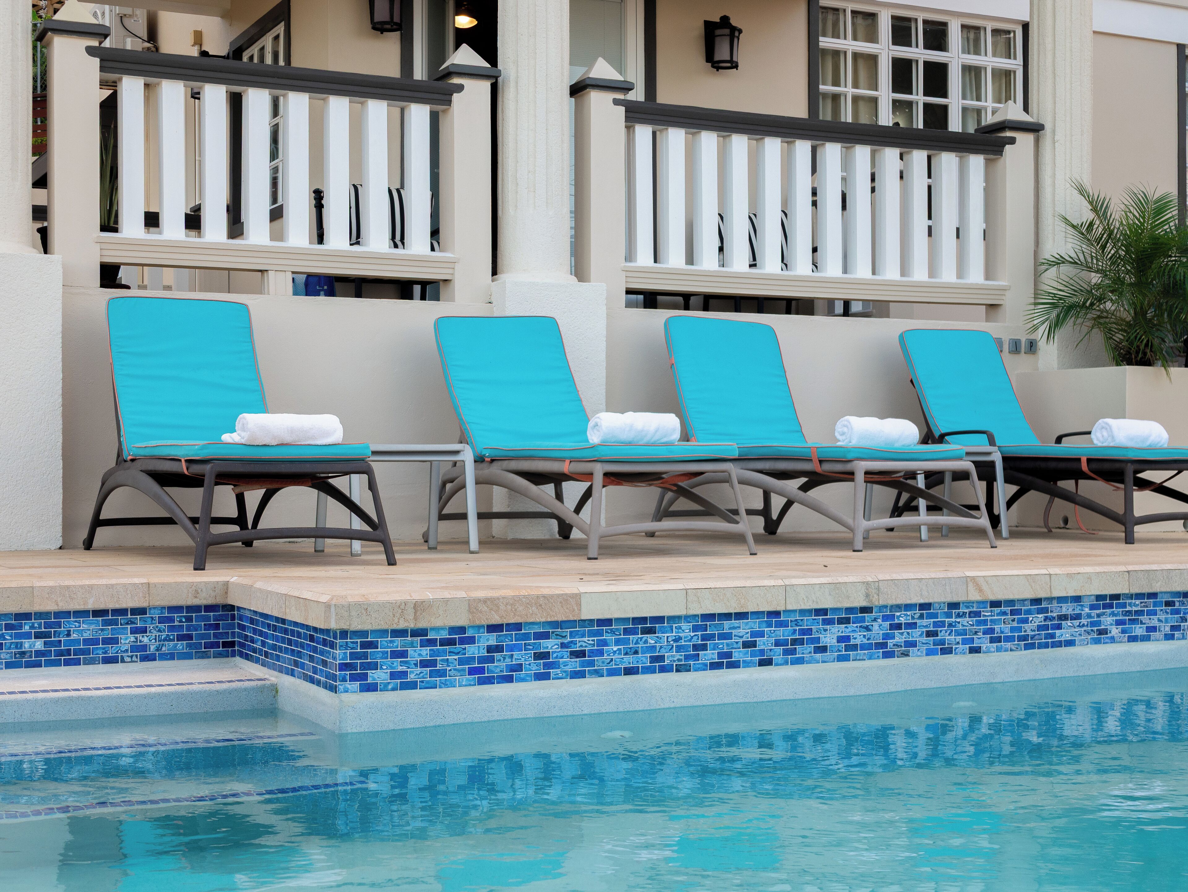 A poolside area with four lounge chairs, a tiled pool edge, and a white railing.