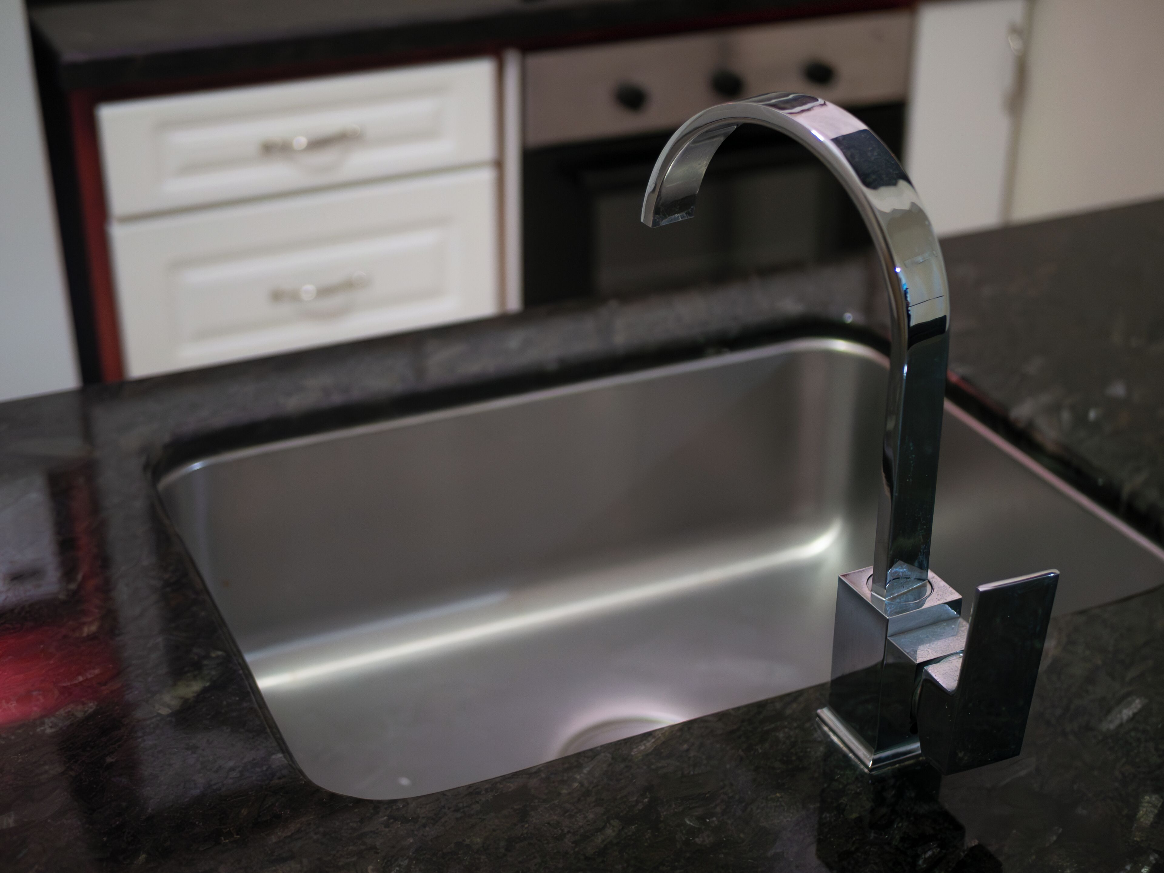 A kitchen sink with a modern faucet, a stainless steel basin, and a black granite countertop.