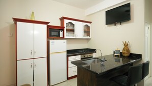 Una cuina moderna amb armaris blancs, tauleig negre i microones integrat. Hi ha una petita illa amb tamborets i una decoració amb pinya.