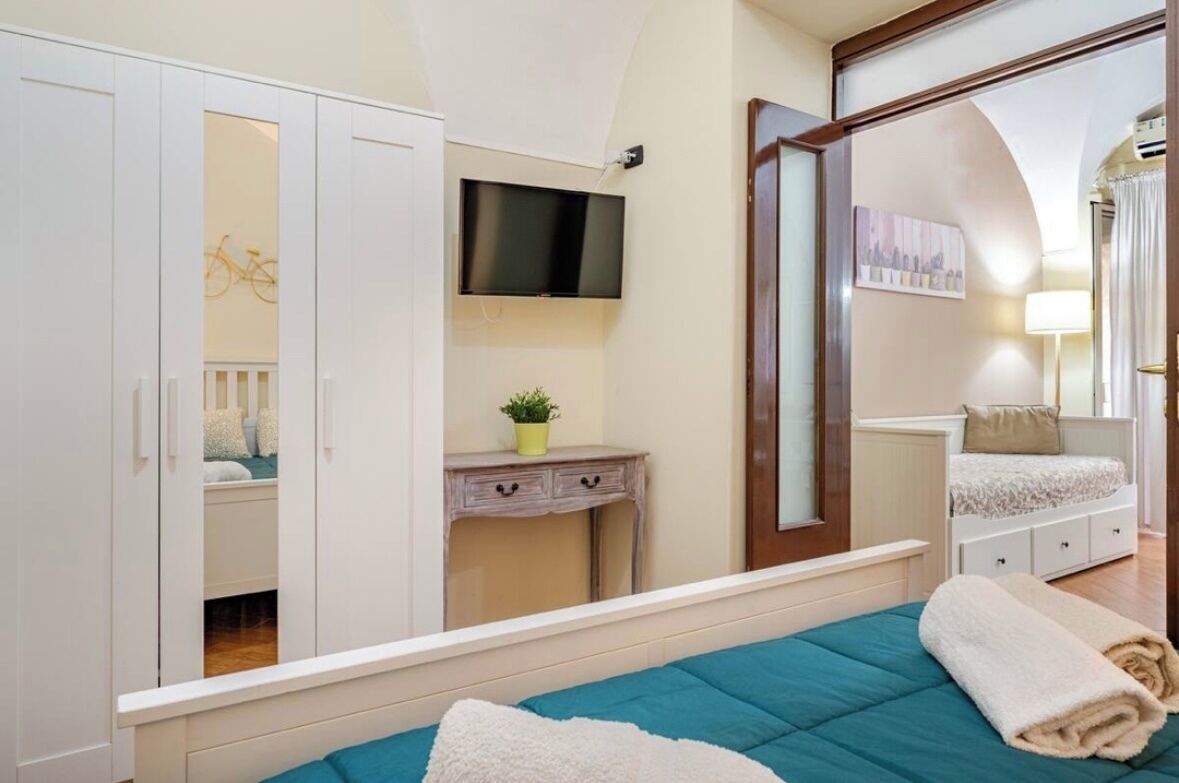 A bedroom with a bed, a TV, a wardrobe, a desk, and a mirror.