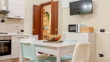 Una cucina compatta con zona pranzo, una TV fissata al muro e una porta in legno che dà su un'altra stanza.