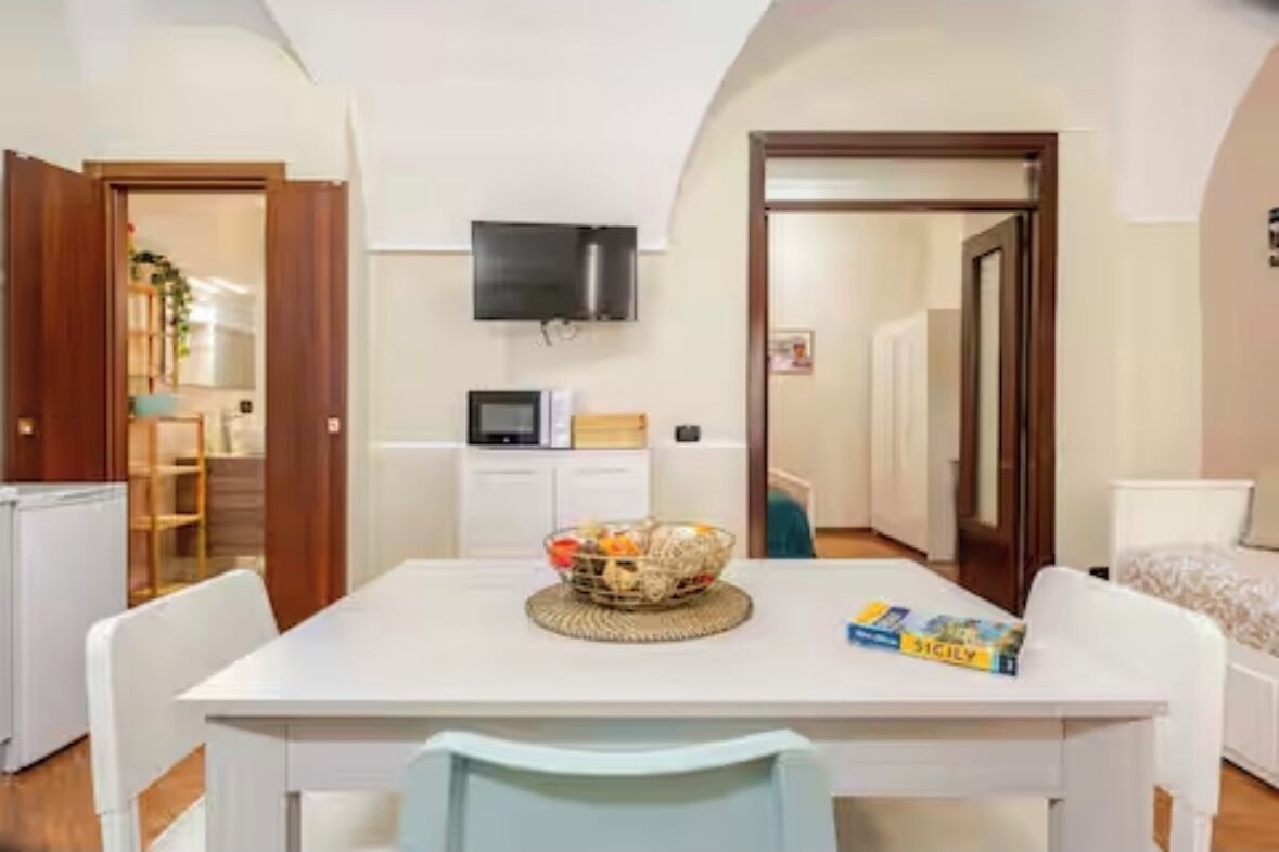 A compact room with a white table, a television mounted on the wall, and a door leading to another room.