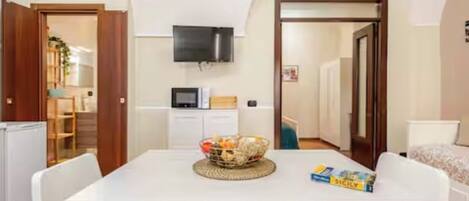 Una habitación pequeña con una mesa blanca, un televisor en la pared y una puerta que da a otra estancia.
