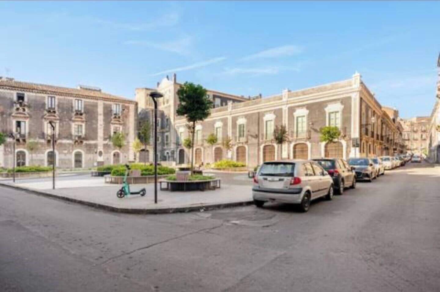 A street with parked cars and a pedestrian area with a bench.