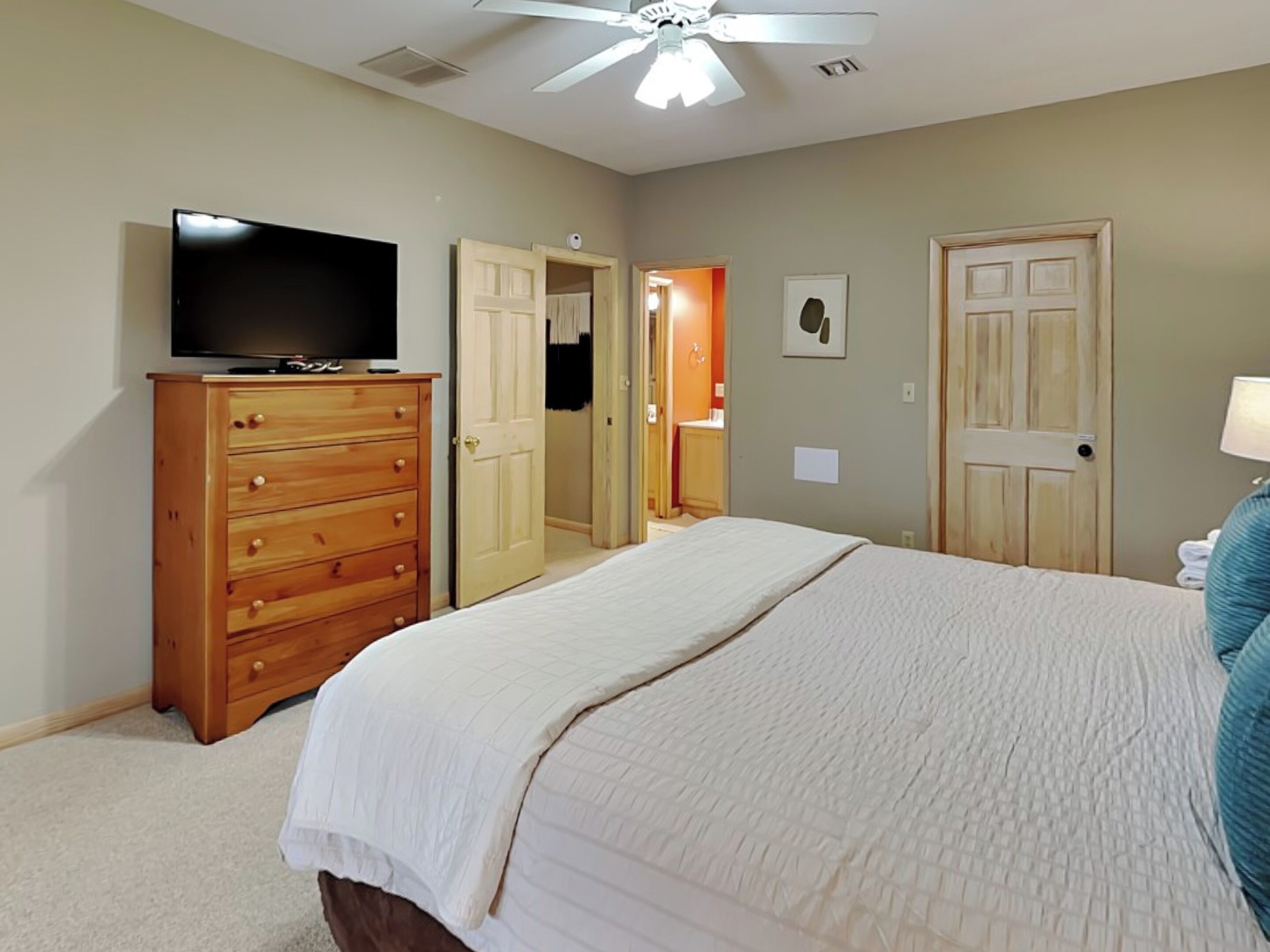 A bedroom with a bed, a wooden dresser, a television, and a ceiling fan.