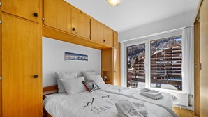 A bedroom with two beds, wooden cabinets, a large window with a mountain view, and a framed picture on the wall. - Christiania I A8 - 6 pers - ski in&out (Haute-Nendaz)