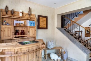 A wooden reception desk with a framed welcome sign, a staircase with metal railings, and a small bench with decorative sheep figures. - Apartment 'Landhaus Zeller 2 Schlafzimmer' with Mountain View, Shared Garden and Wi-Fi (Fügenberg)