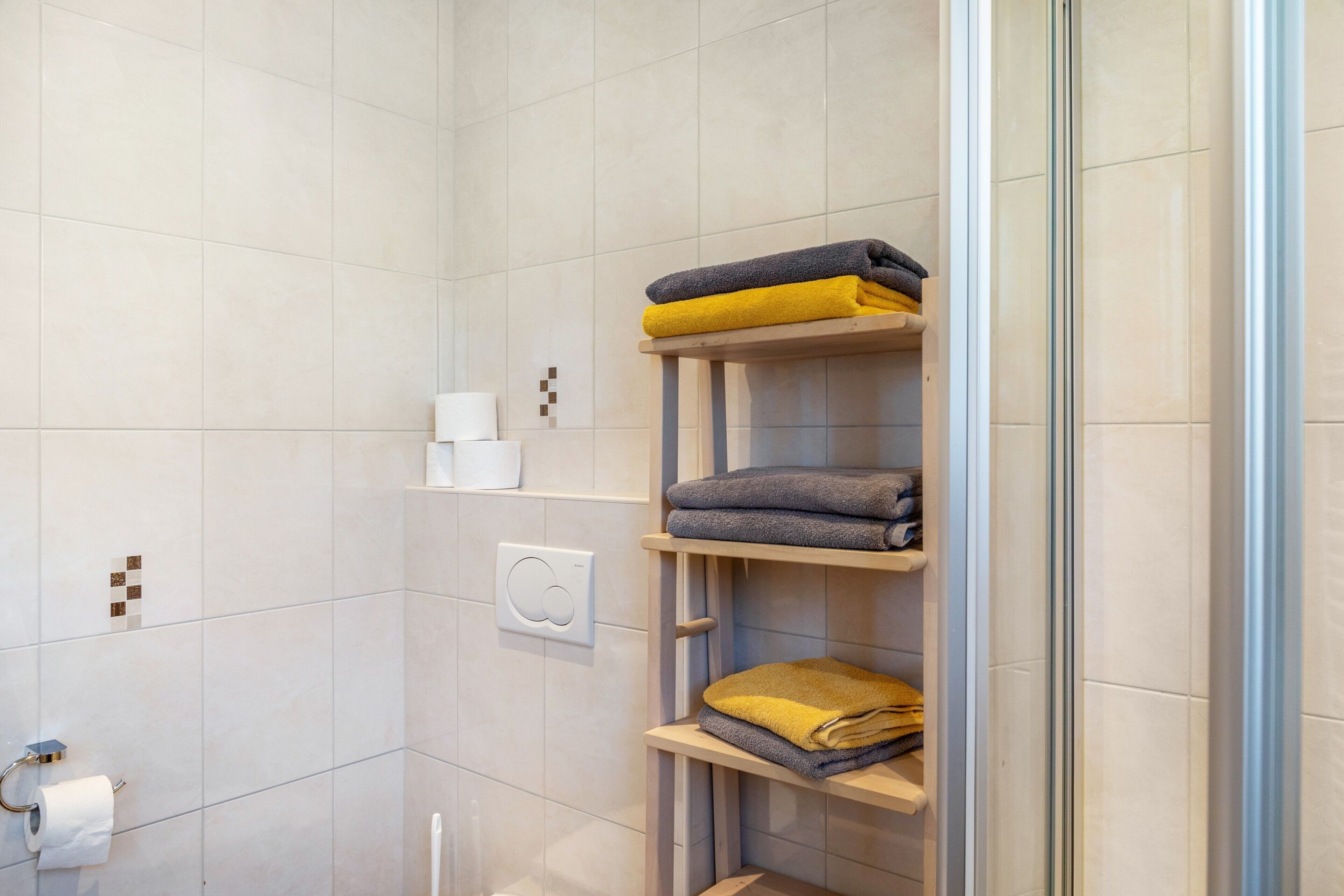 A bathroom with a toilet, a towel rack with folded towels, and a shower area.
