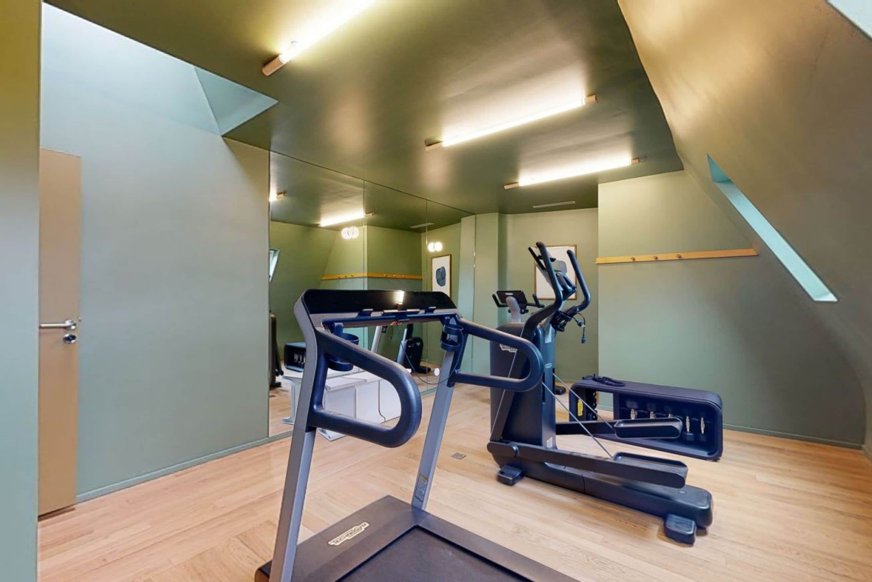 A gym with treadmills, exercise bikes, and a mirrored wall.