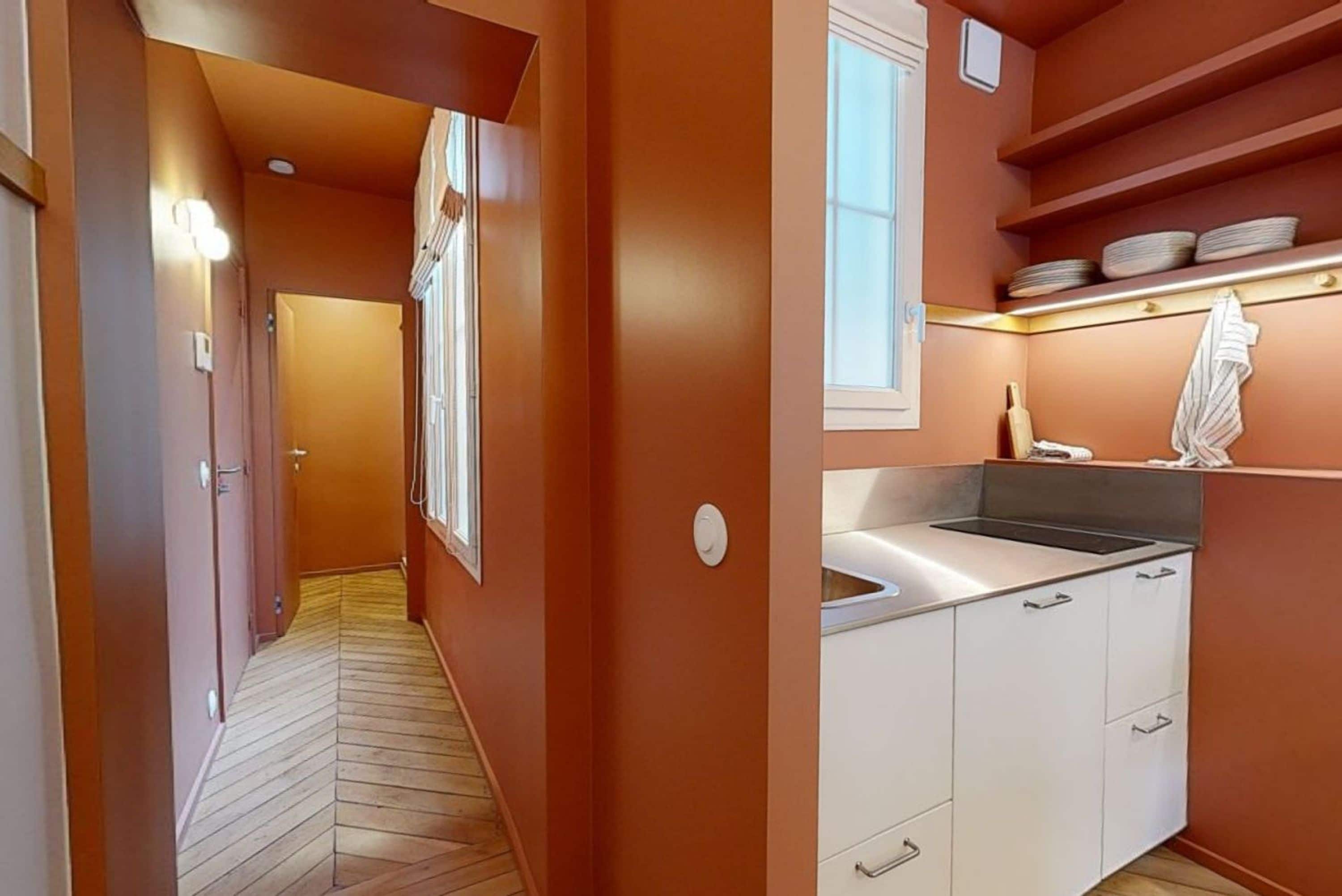 A narrow hallway with wooden flooring leading to a kitchen area with white cabinets and a sink.