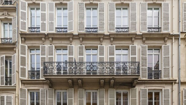 A multi-story building with uniform window shutters and decorative iron railings on balconies. - Joivy Delightful 1-bed Studio w/ Shared Co-working (Paris)