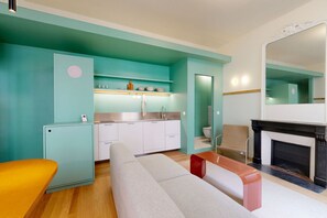 Un salon moderne comprenant un canapé, une petite table, un coin cuisine avec un évier et des placards, ainsi qu’une cheminée.